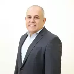 Um homem de terno e camisa branca está parado em frente a um fundo branco.