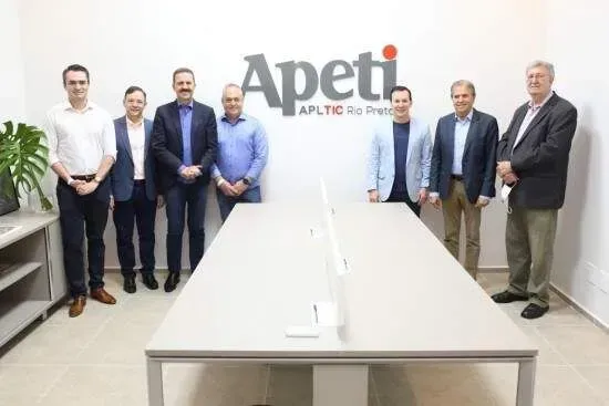 Um grupo de homens está de pé em frente a uma mesa com a palavra apeti na parede atrás deles.