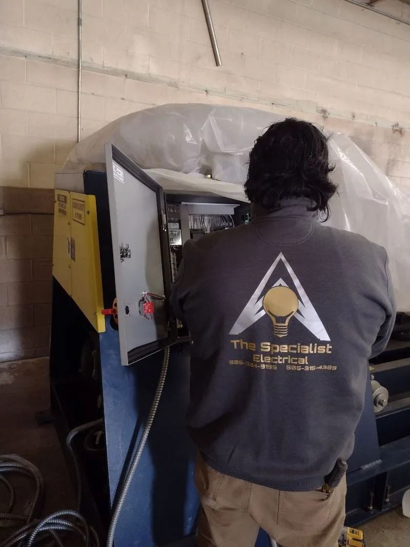A technician in a grey company-branded sweatshirt works on the open electrical panel of an industrial machine.