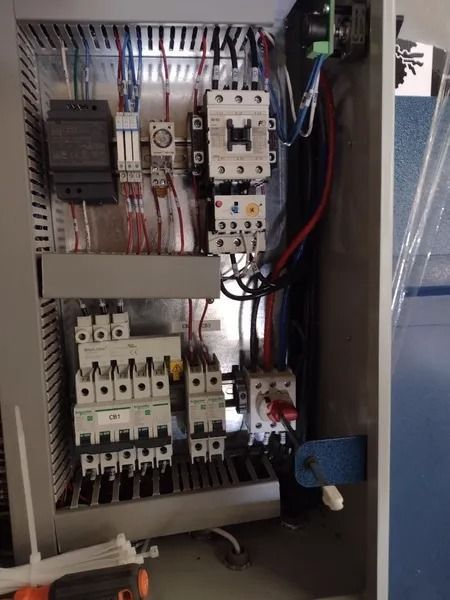 An open electrical control panel box featuring various circuit breakers, a contactor, and wiring against a metallic back.