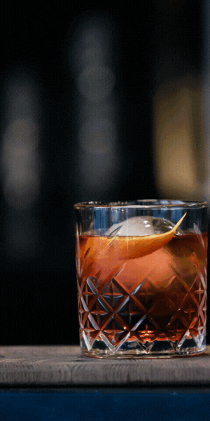 Crystal whiskey glass with amber drink and ice on a dark table