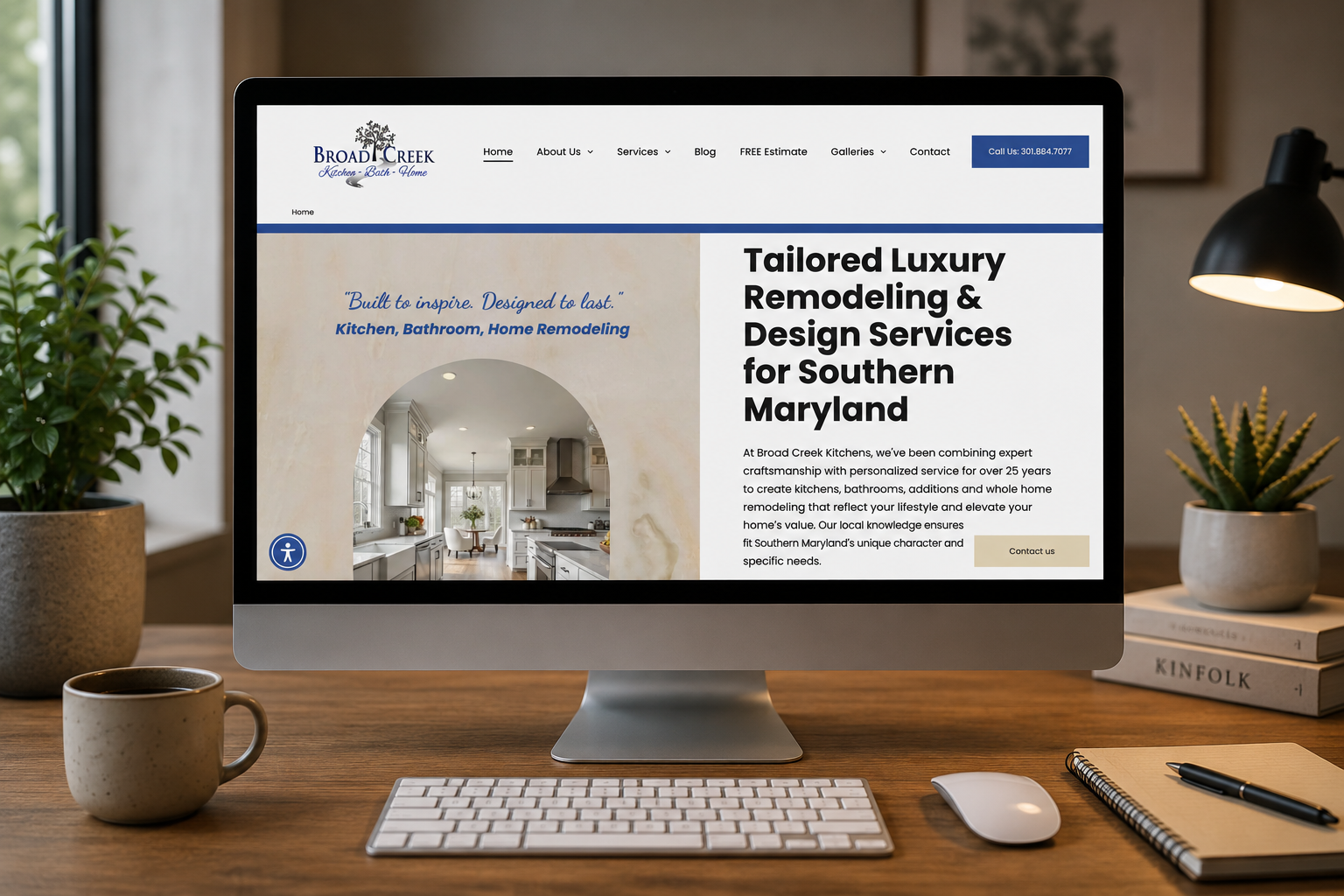 Desk with iMac showing a luxury remodeling website for Southern Maryland, beside keyboard, mouse, coffee and lamp