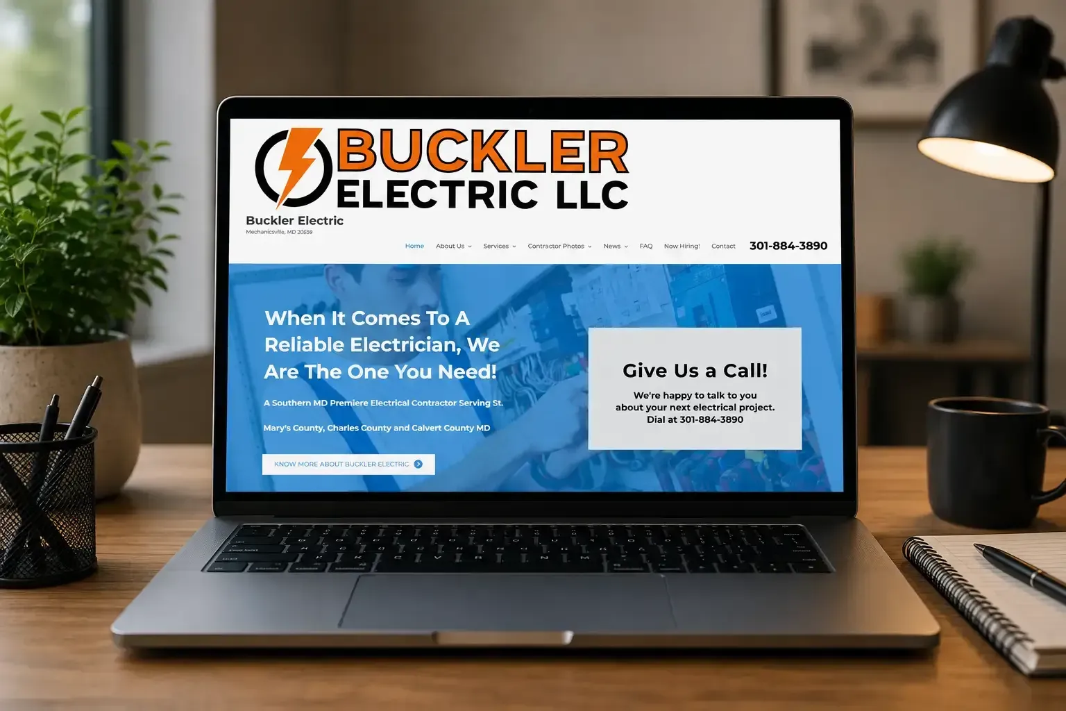 Laptop displaying Buckler Electric LLC website on a desk with notebook and lamp