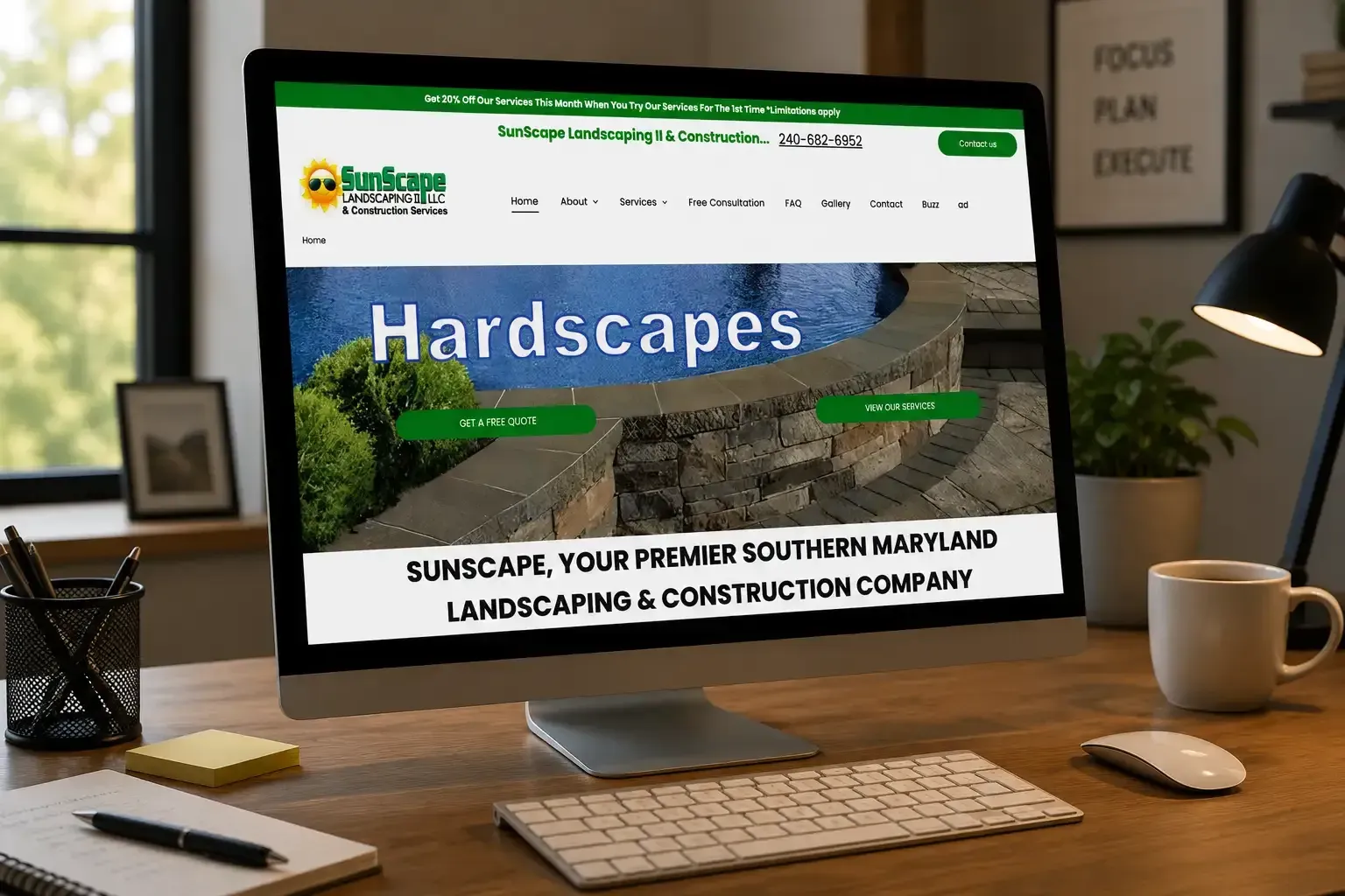 Computer displaying a landscaping website on a desk with keyboard, mouse, mug, and lamp