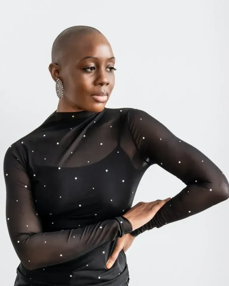Person in a sheer black top with silver dots posing against a light background