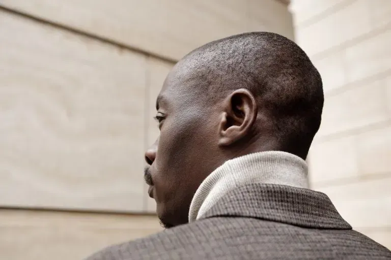 Rear view of a man in a gray suit looking toward a beige wall outdoors