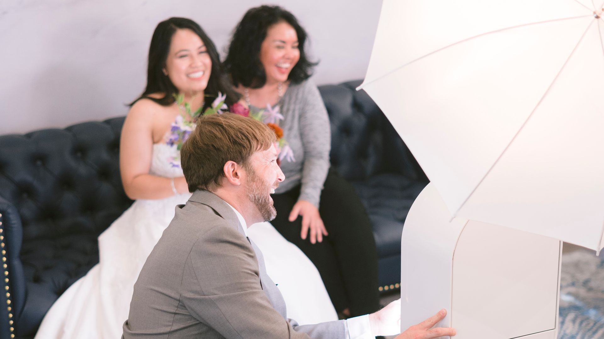 Three people pose for a photo in a bright studio, seated on a dark couch behind a white umbrella light.