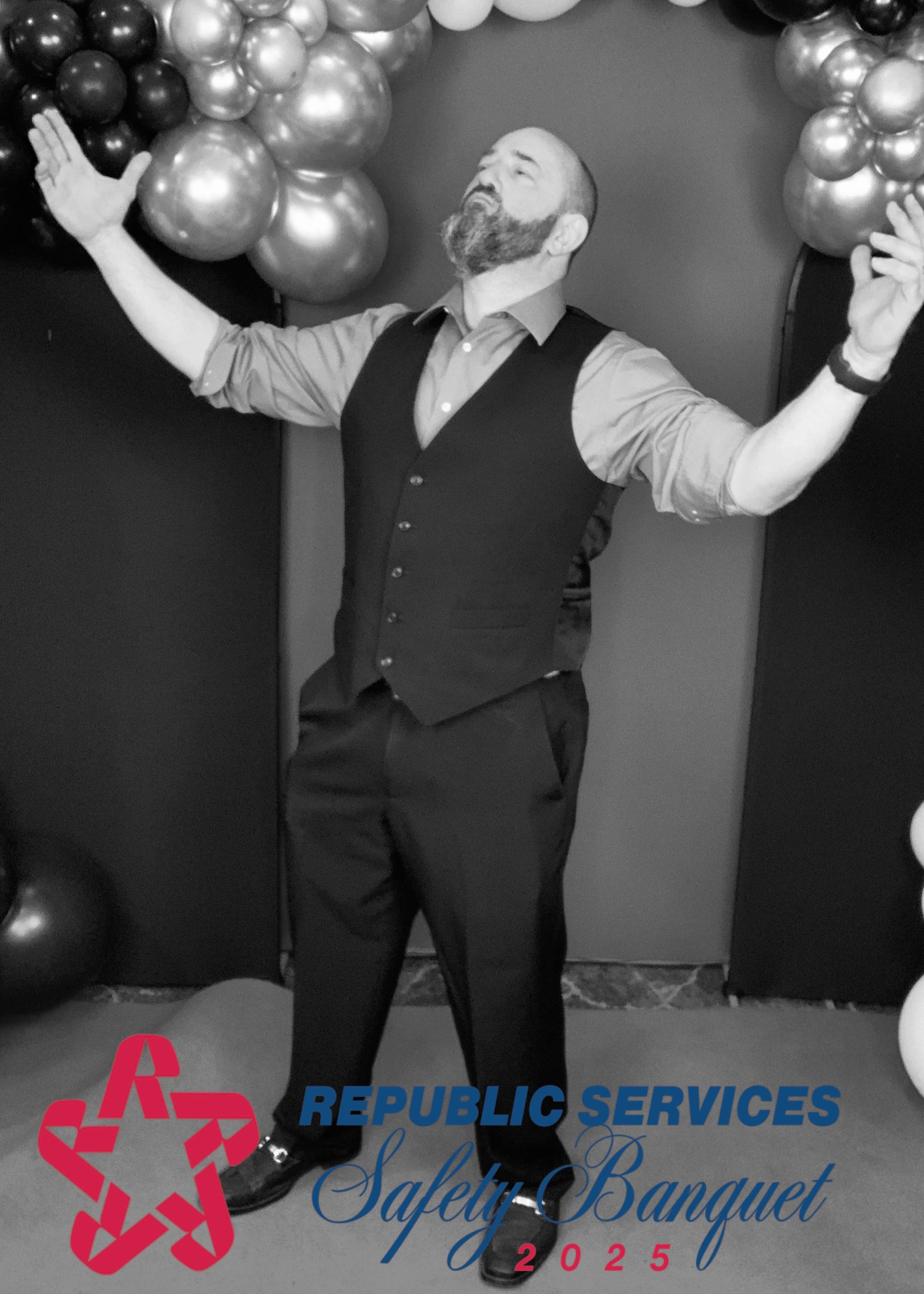 Man celebrating with arms raised between balloon clusters at a Republic Services Safety Banquet backdrop
