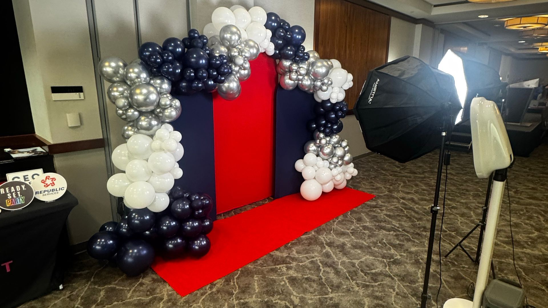 Balloon arch around a red backdrop and carpet, with studio lights in an indoor event space.