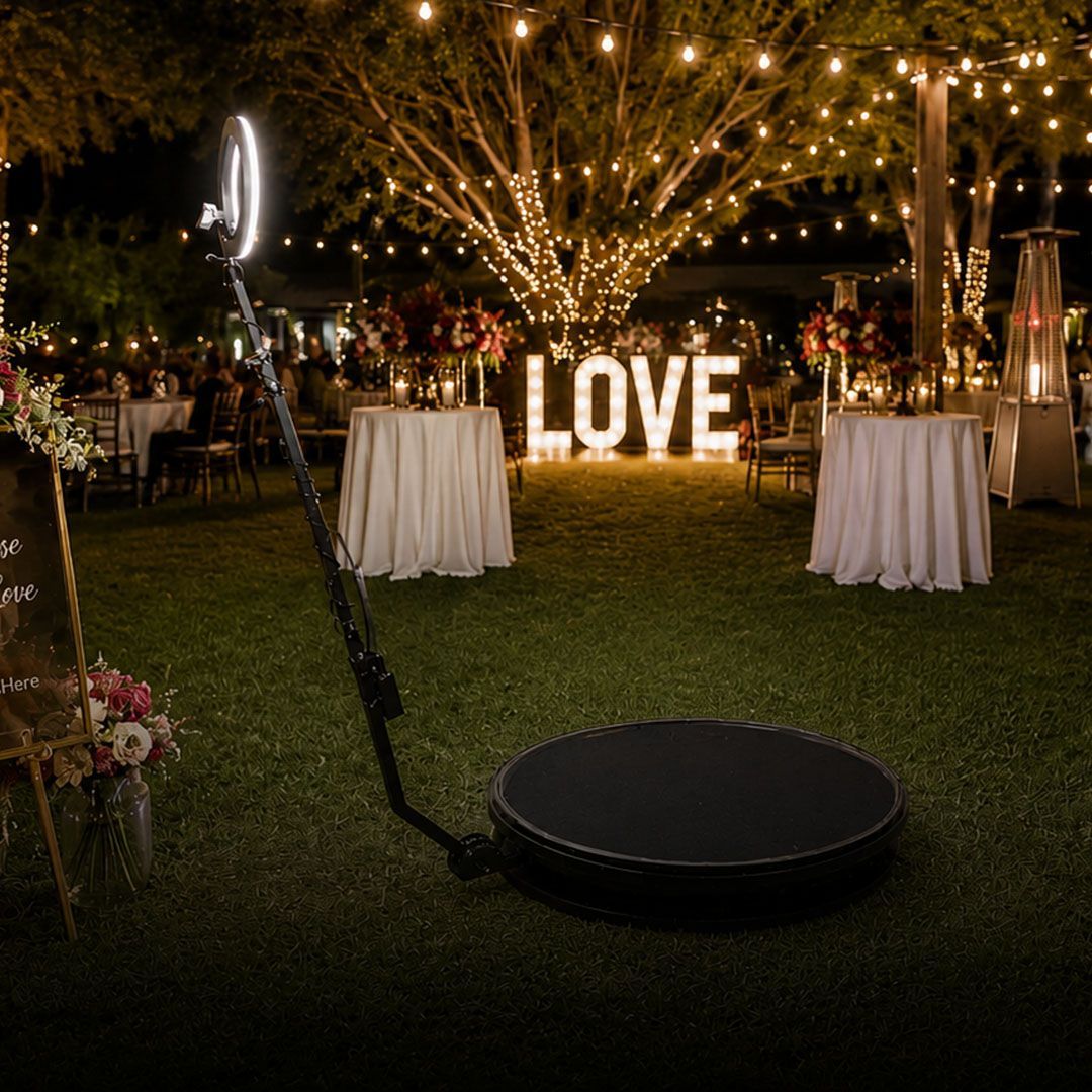 Outdoor wedding reception at night with glowing “LOVE” sign, lit trees, and cocktail tables on a lawn
