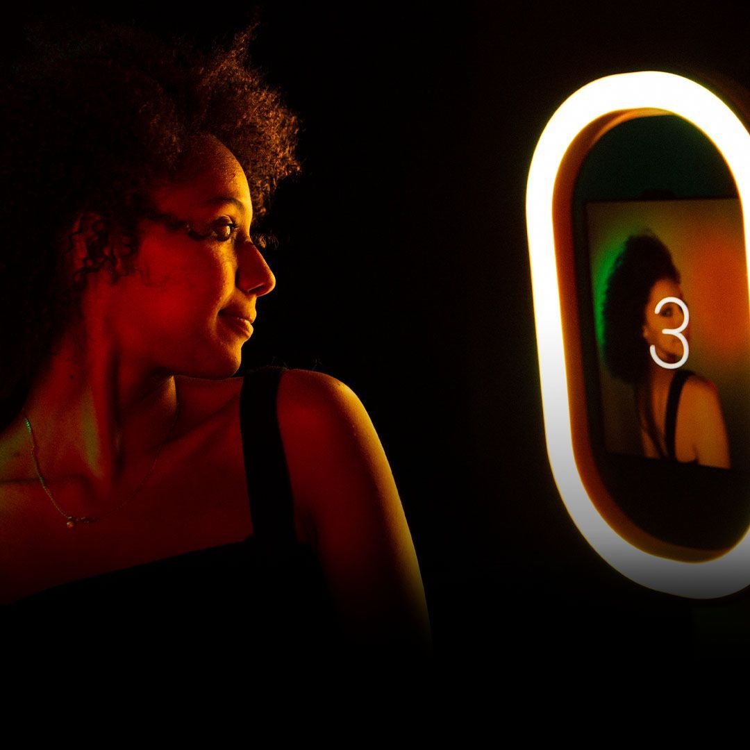Person lit in red looking at a glowing ring light mirror in a dark room