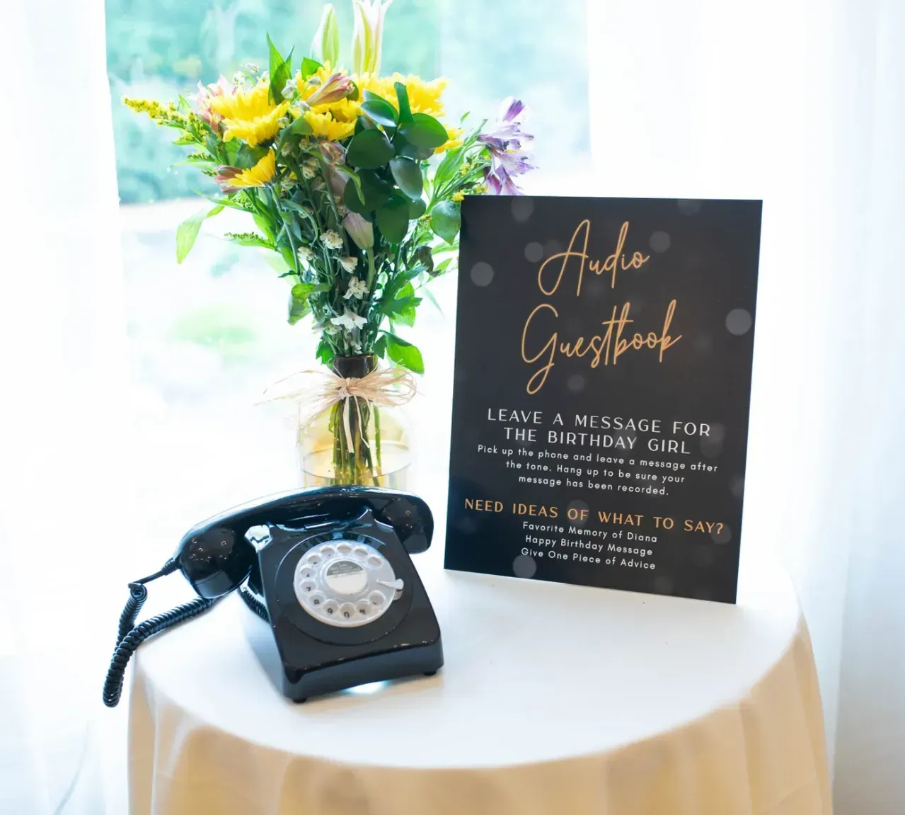 Vintage black rotary phone and floral bouquet beside a black sign on a round table.