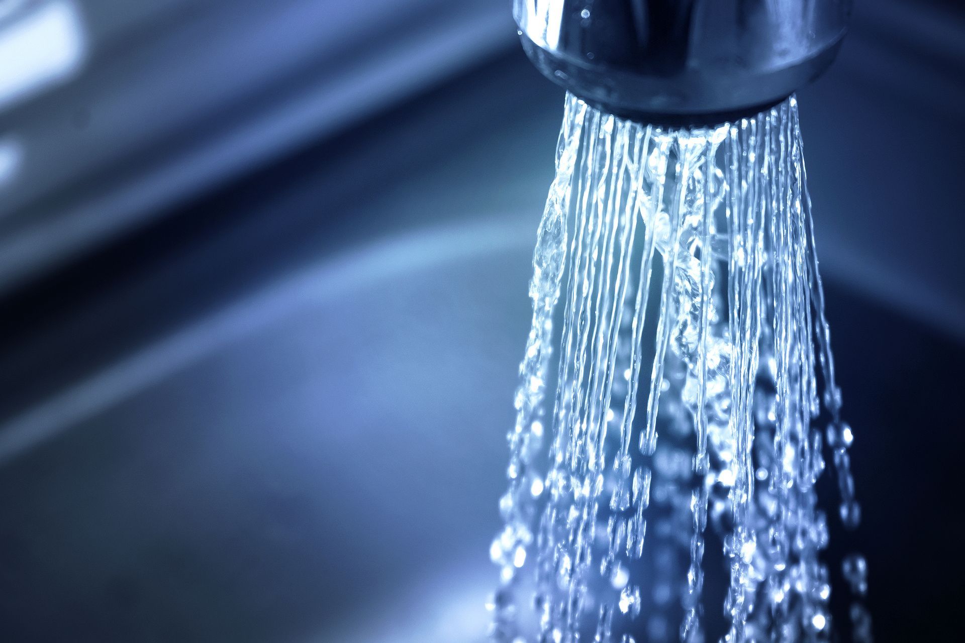 Water flowing from a chrome kitchen faucet into a dark sink.