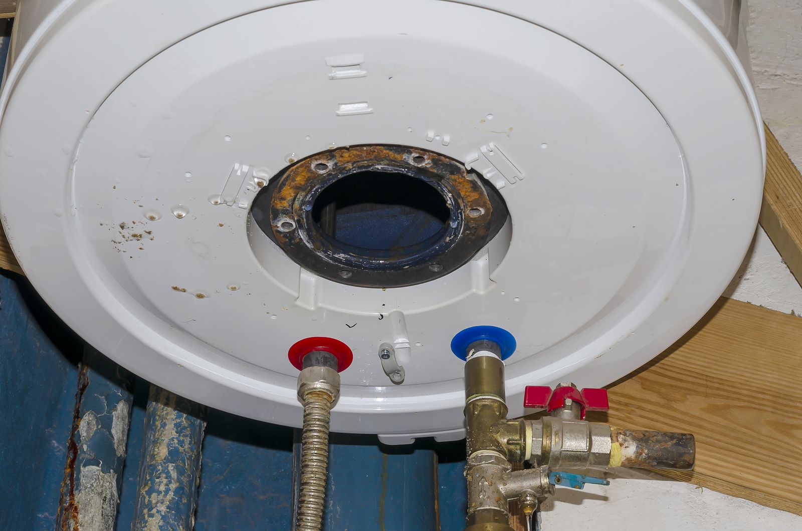 Bottom view of a white water heater tank with a central circular opening, red and blue pipe connections, and brass valves.
