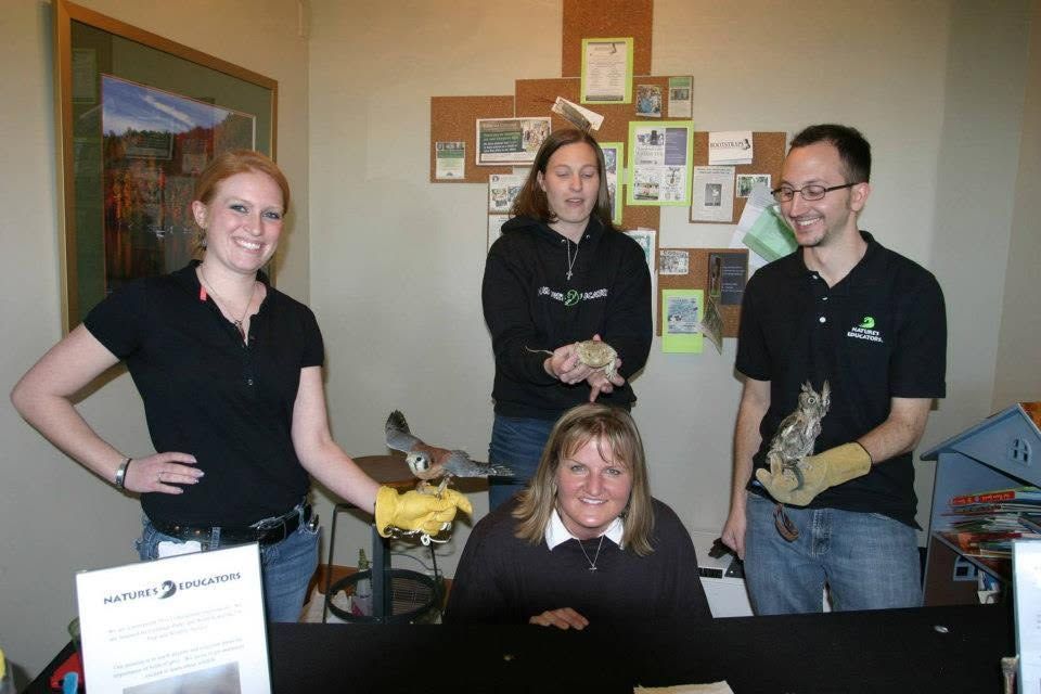 Four people posing in an office, with two holding small animals and a computer desk in front.