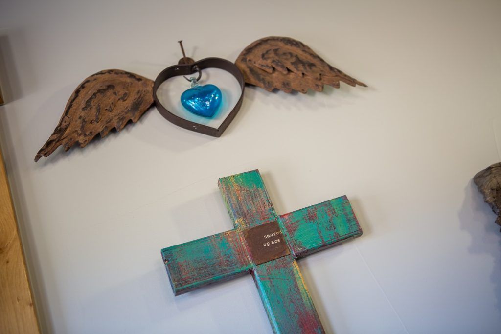 Wall decor with a heart and blue glass wings above a colorful cross on a white wall