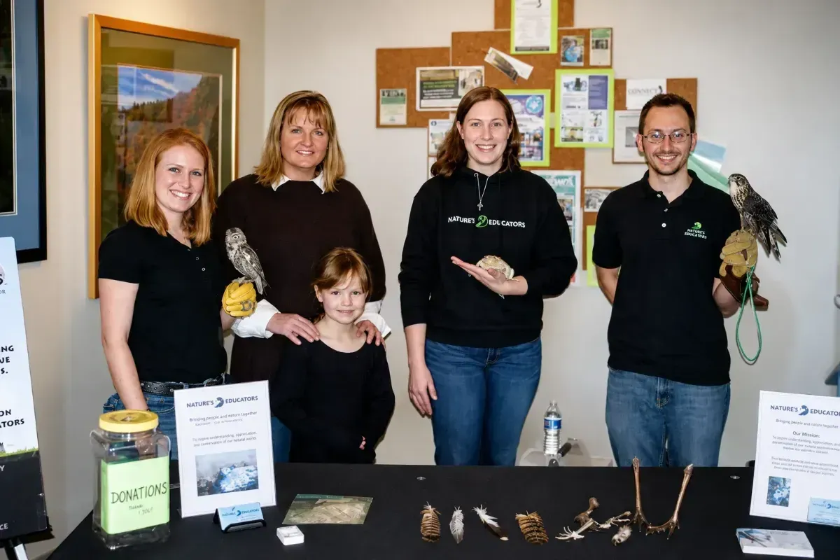 Four people behind a display table with birds and educational materials at an indoor exhibit