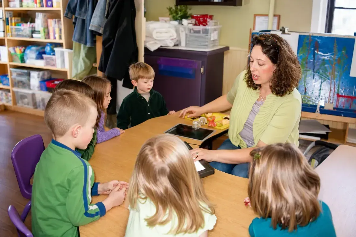 Teacher and children seated around a table, preparing food in a classroom.