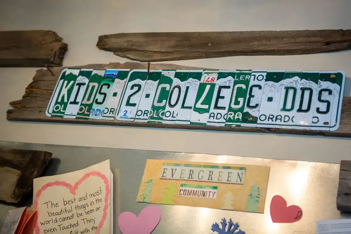 Green and white sign reading “KIDS COLLEGE DDS” mounted on a wood wall with children’s artwork below