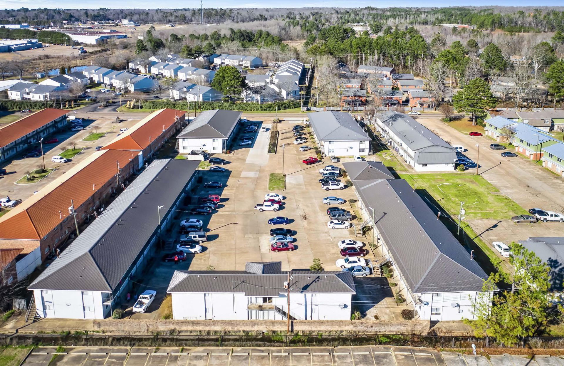 Aerial view of apartment buildings and parking lots in a residential complex with trees nearby