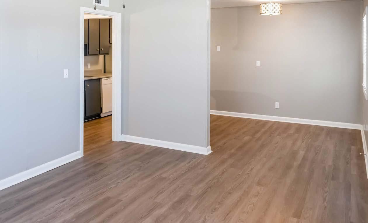 Empty living room with gray walls, wood floors, and a view into the kitchen