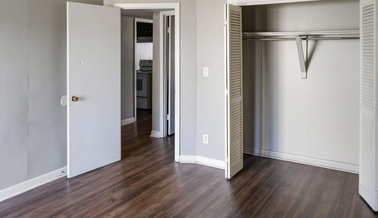 Empty bedroom with open closet, white walls, and wood flooring