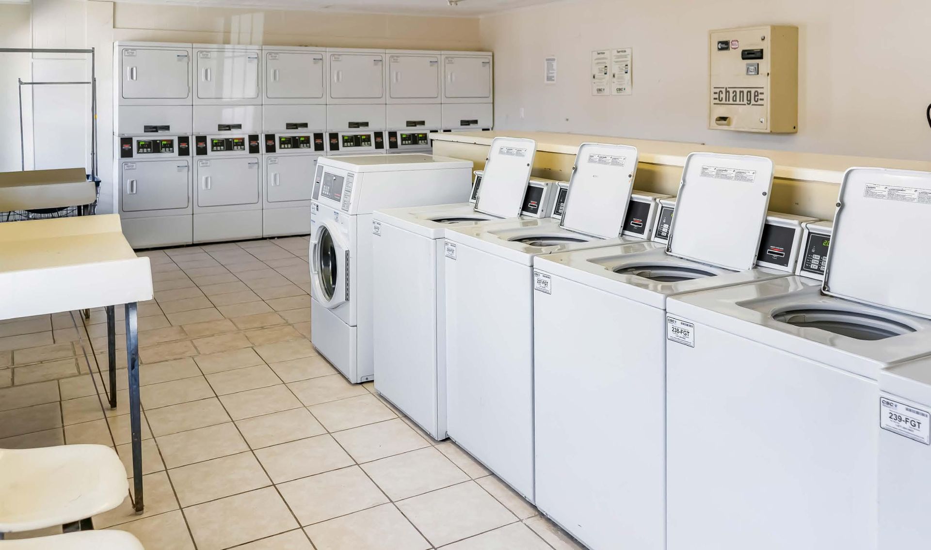 Laundry room with white washers and dryers lined against the wall on a tiled floor