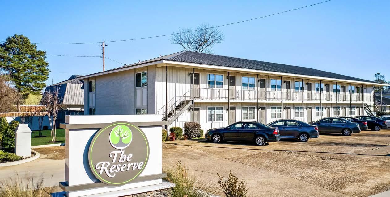 The Greensy sign in front of a beige two-story apartment building with parked cars