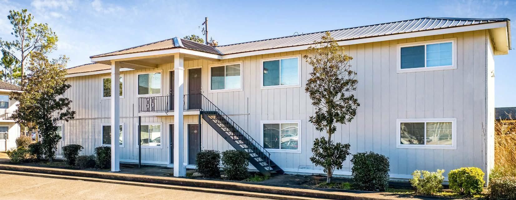 Two-story white apartment building with blue trim and exterior stairs in sunlight