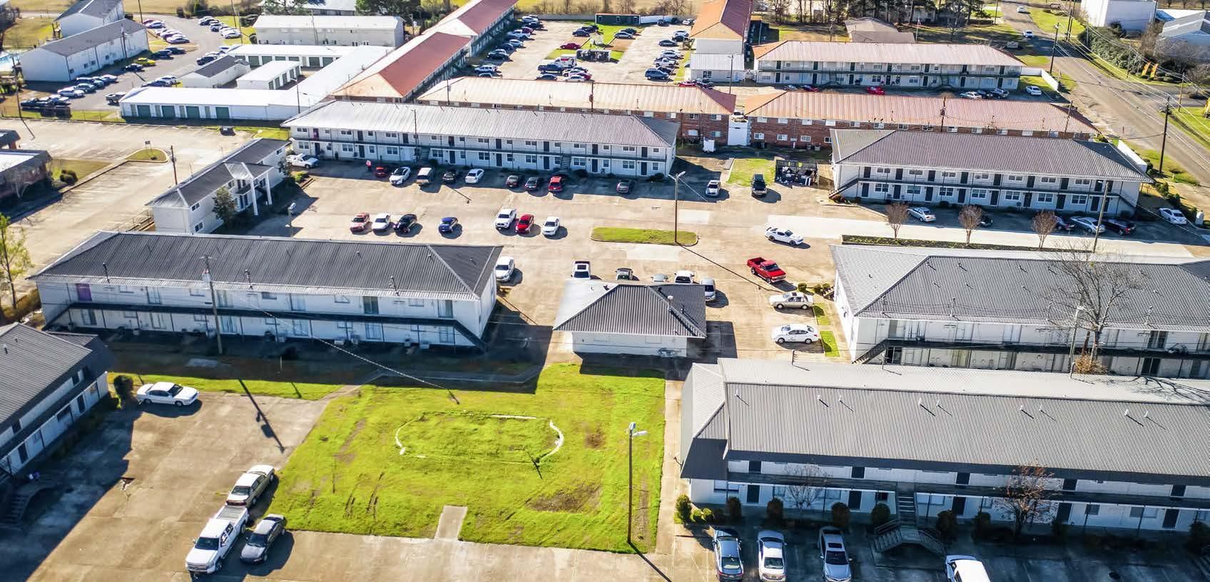 Aerial view of a residential apartment complex with parking lots and green lawns on a sunny day