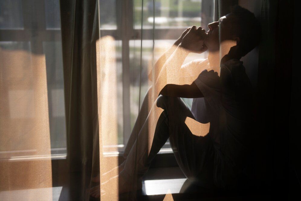 A woman is sitting in front of a window looking out.