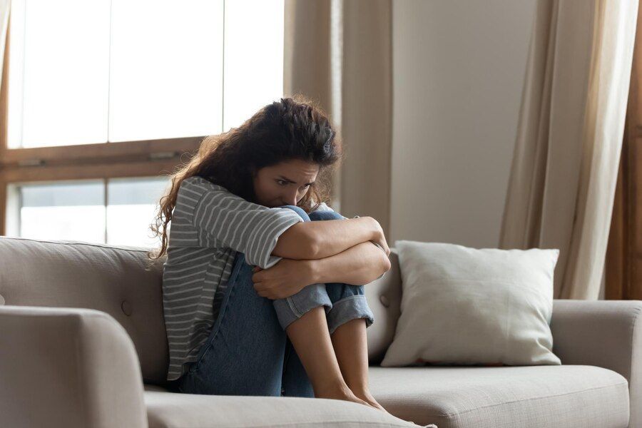 A woman is sitting on a couch hugging her knees.