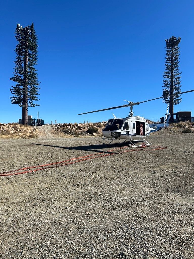 A helicopter is parked in a gravel field next to two trees.