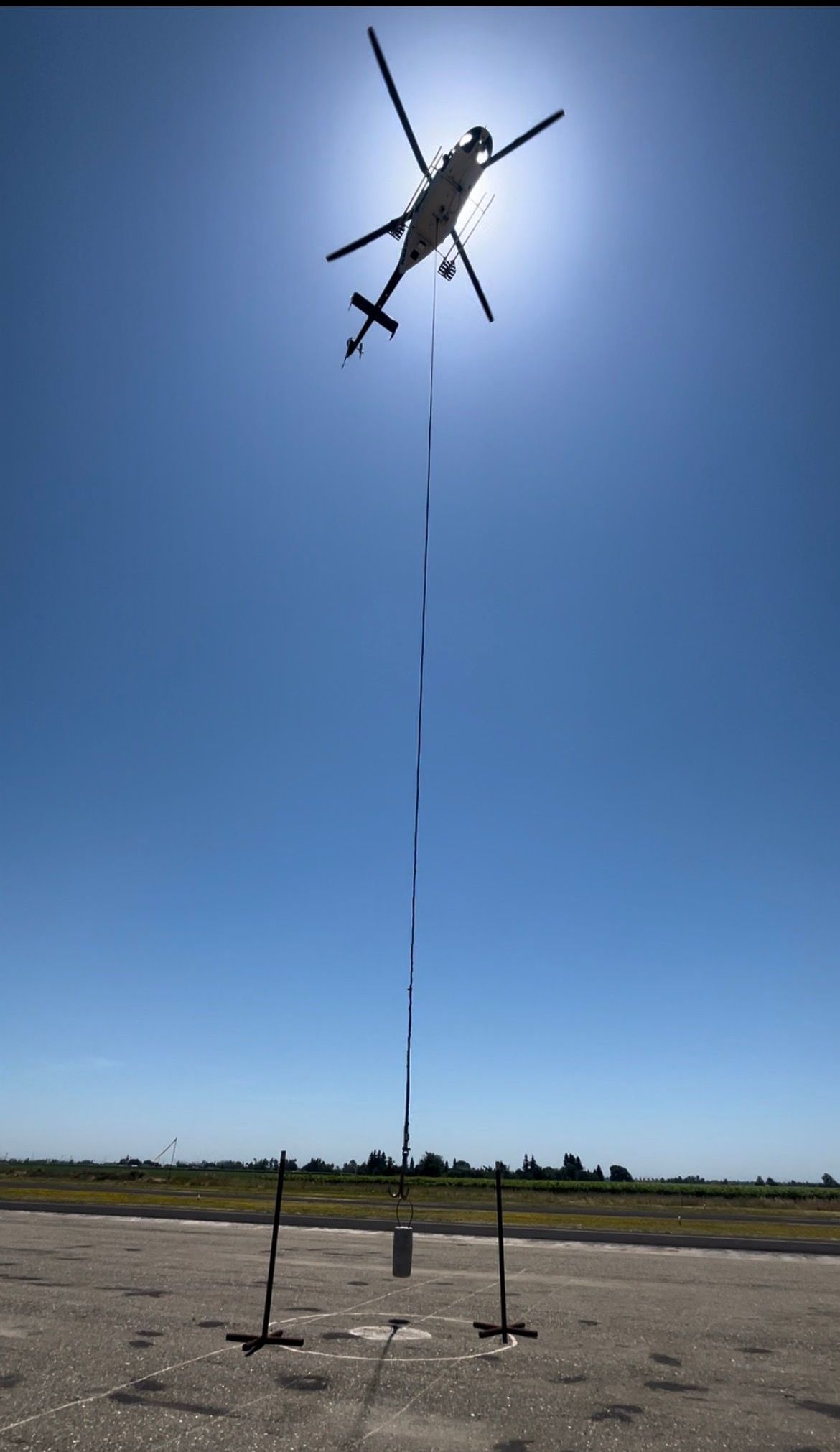 A helicopter is flying over a runway with a rope attached to it