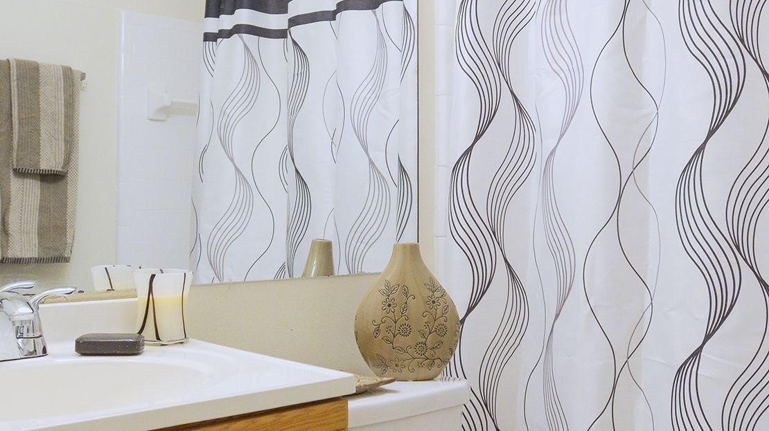 Bathroom sink with a mirror, white lace curtains, and a decorative vase on the counter.