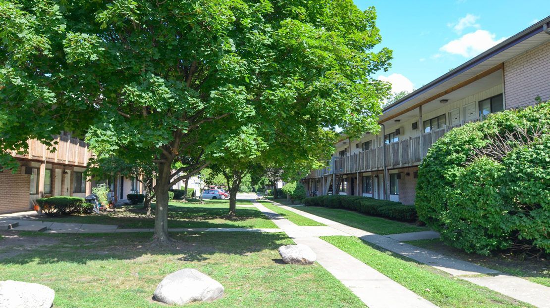 Apartment courtyard with green trees, grass, sidewalks, and two-story buildings on a sunny day