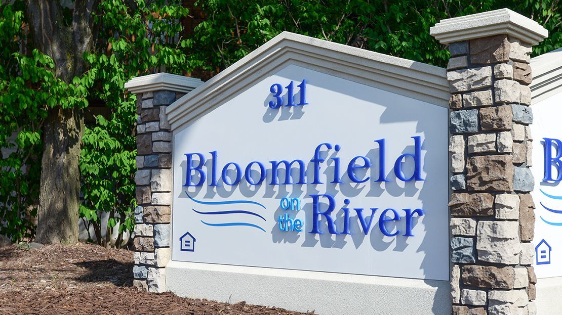 Bloomfield River entrance sign with blue lettering and stone pillars amid greenery