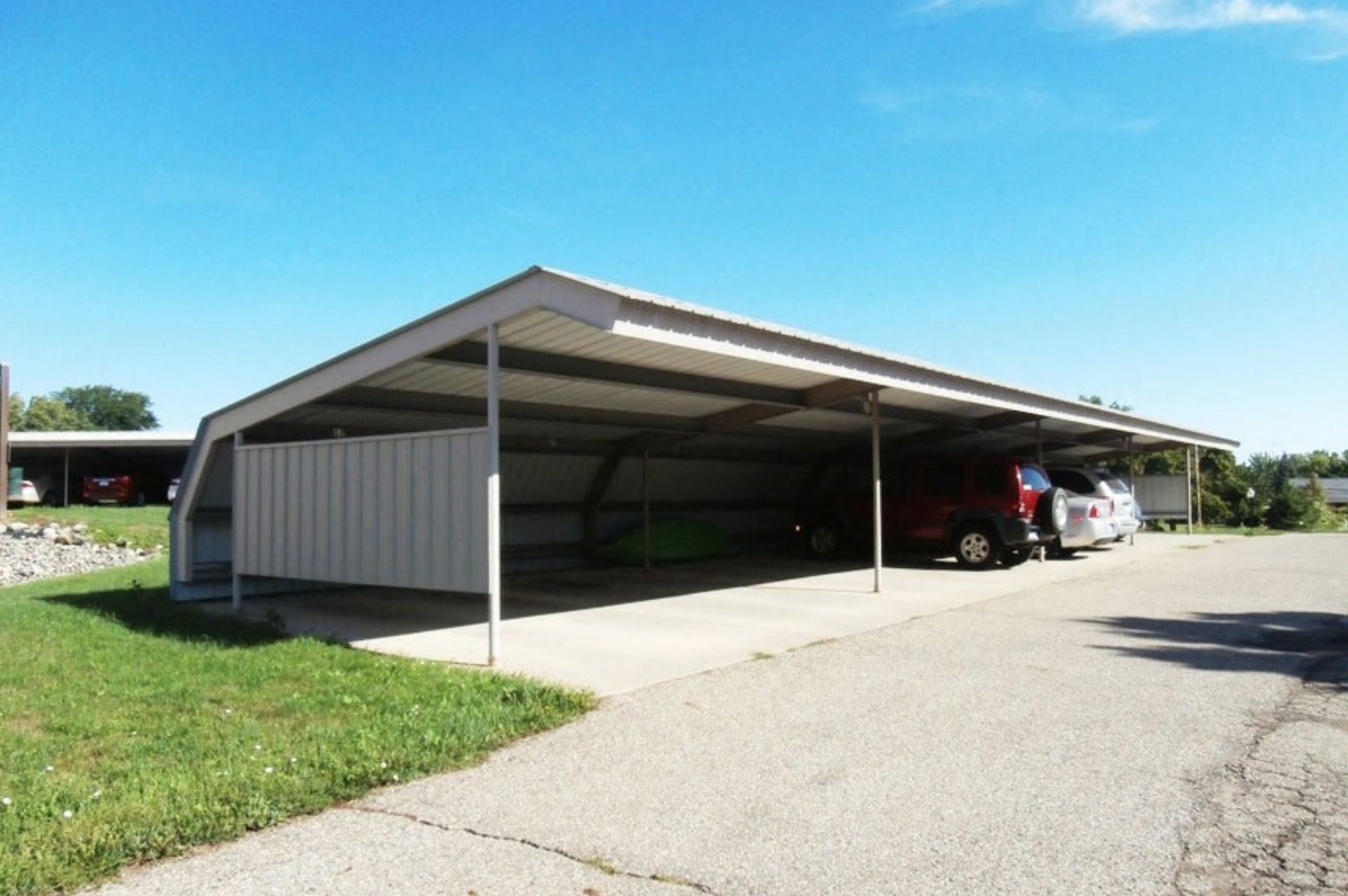 Open carport with a red SUV parked inside beside a paved driveway and green lawn