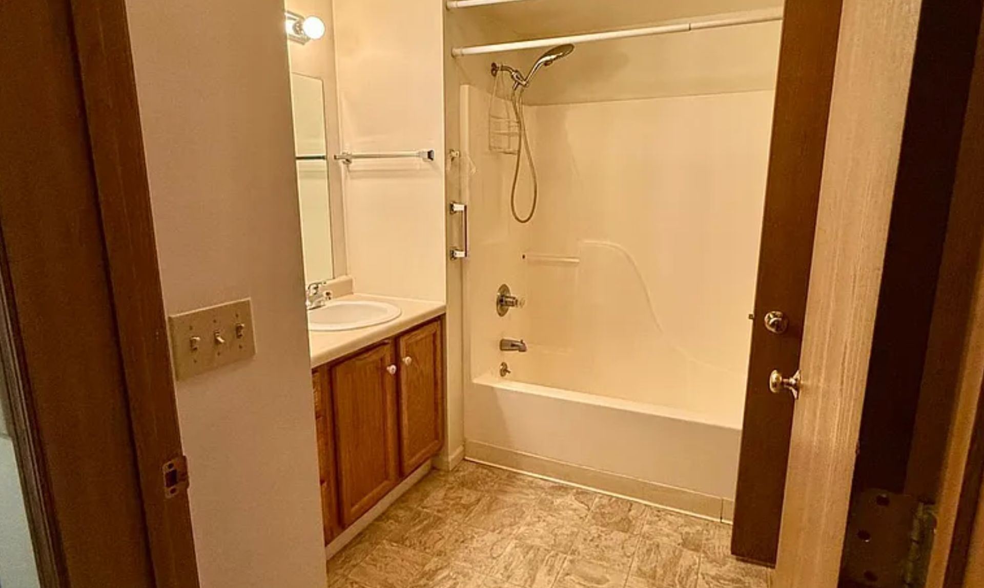 Small bathroom with a tub, vanity, mirror, and beige tile floor viewed through an open doorway