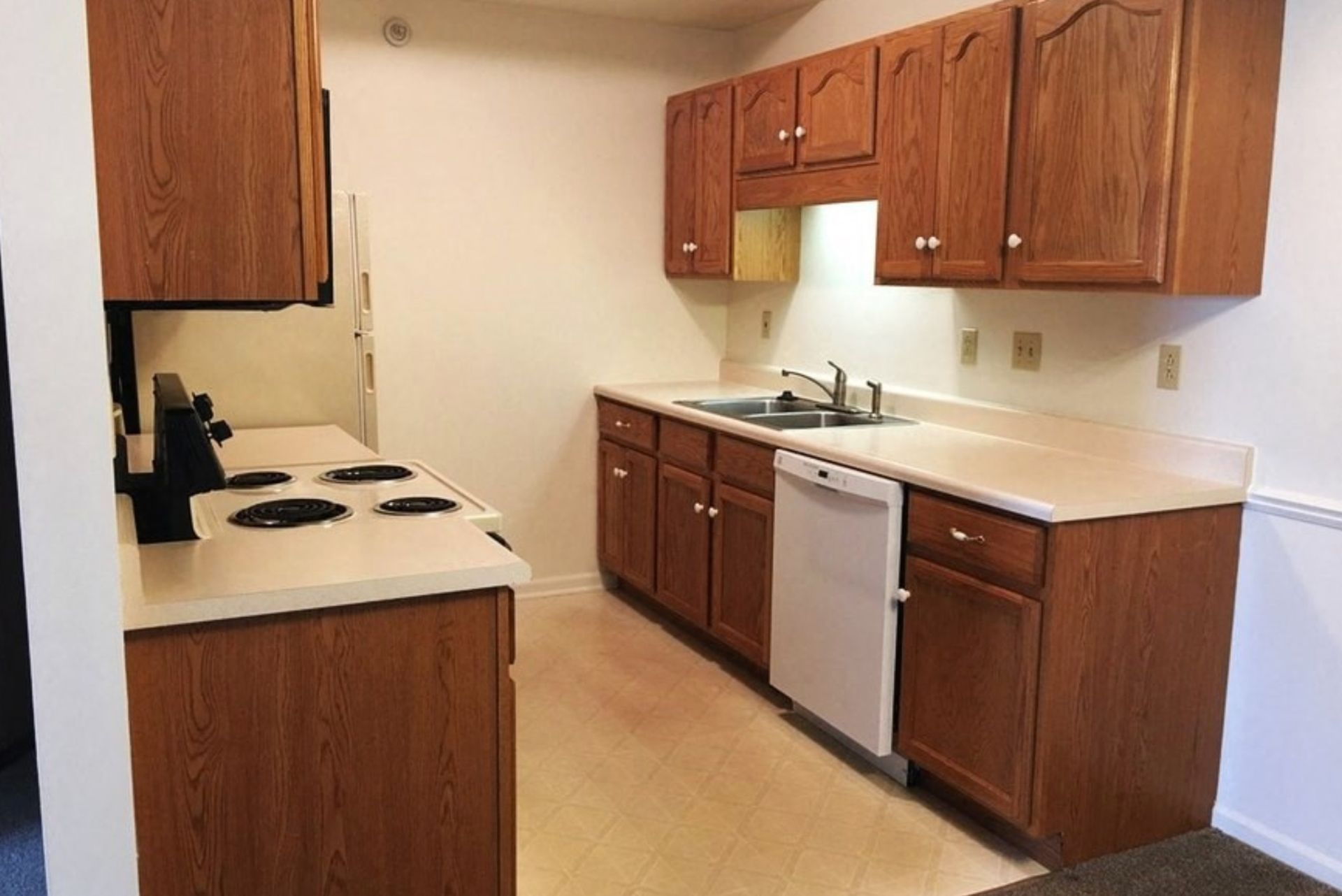Small kitchen with wood cabinets, white countertops, stove, dishwasher, and sink.