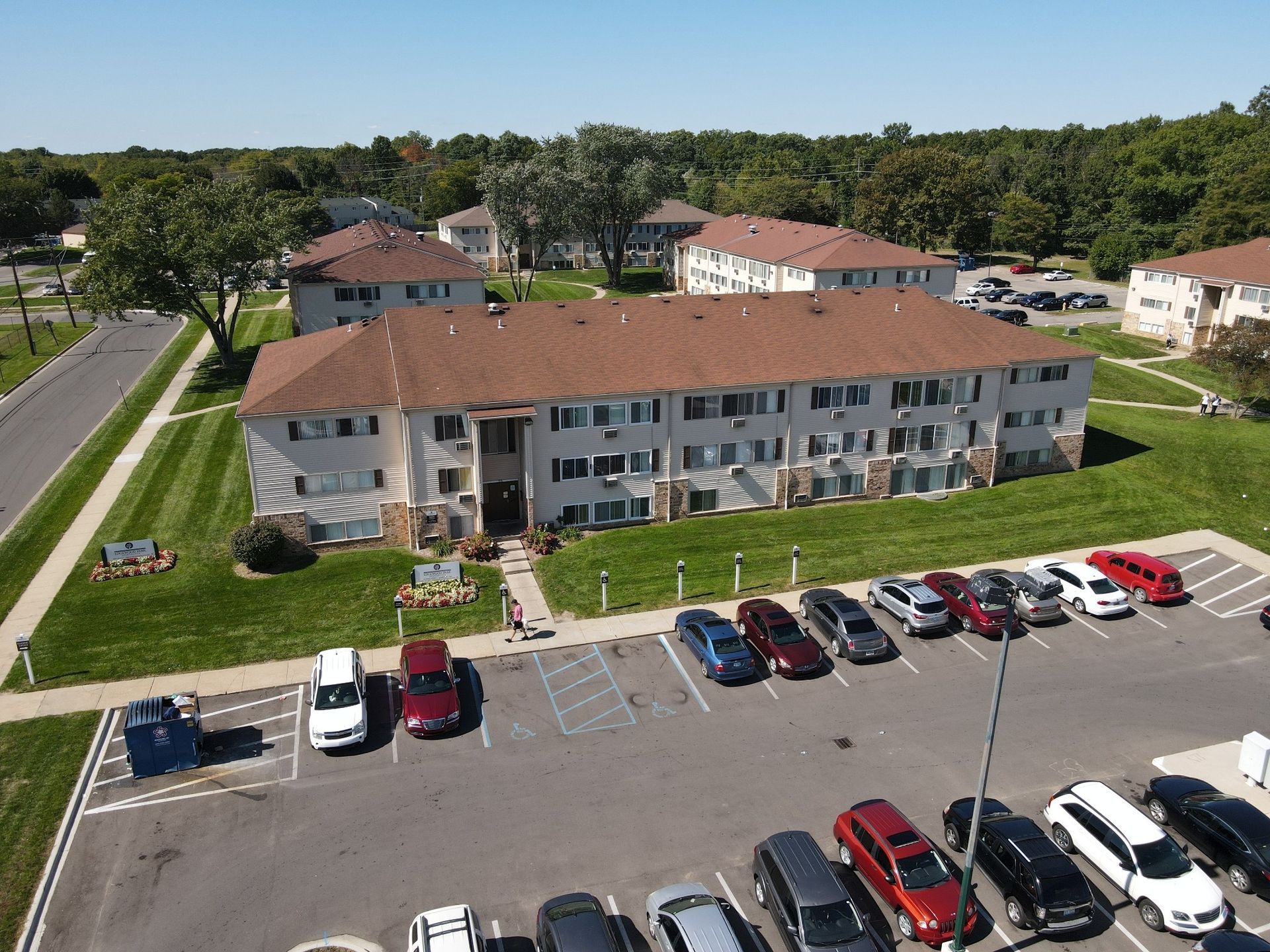 Aerial view of a two-story apartment complex with a parking lot and cars in front.