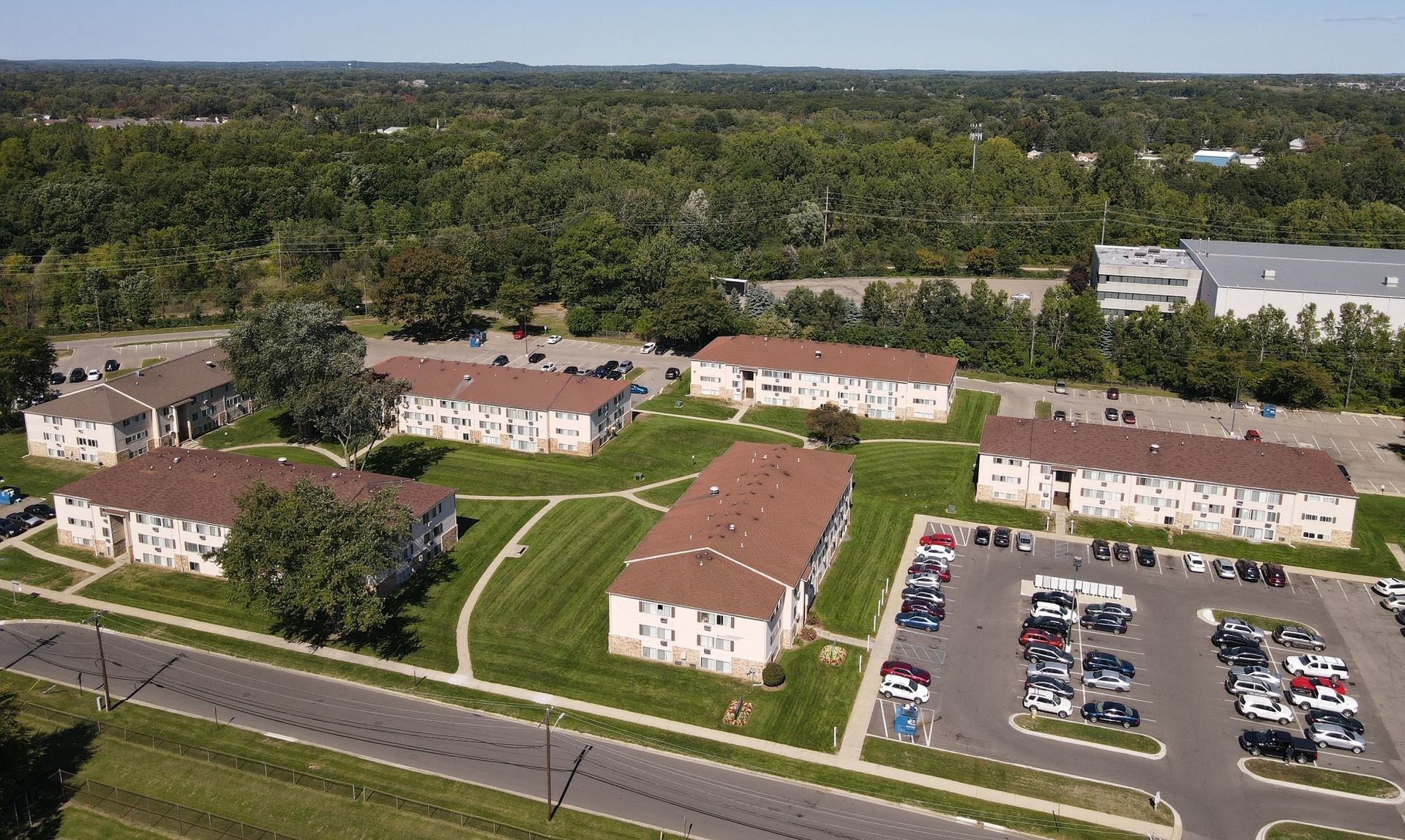 Aerial view of apartment buildings, parking lot, and trees near a road on a sunny day