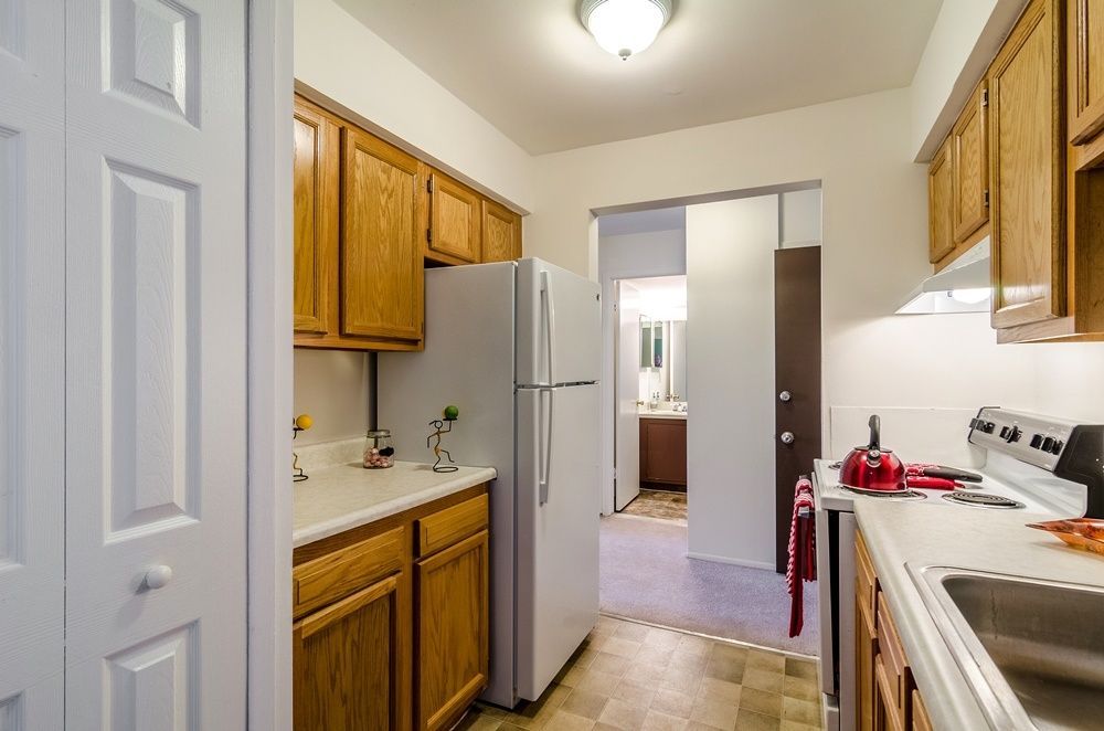 Small galley kitchen with white appliances, wood cabinets, and beige tile flooring.
