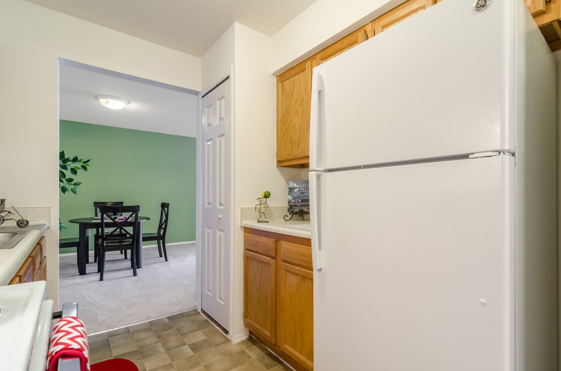 Kitchen view with white refrigerator, wooden cabinets, and dining area beyond a doorway