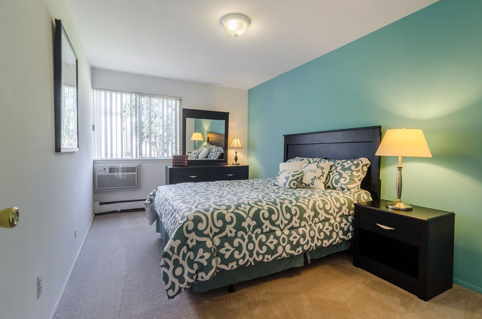 Bright bedroom with patterned bedspread, nightstand lamps, and a window with vertical blinds