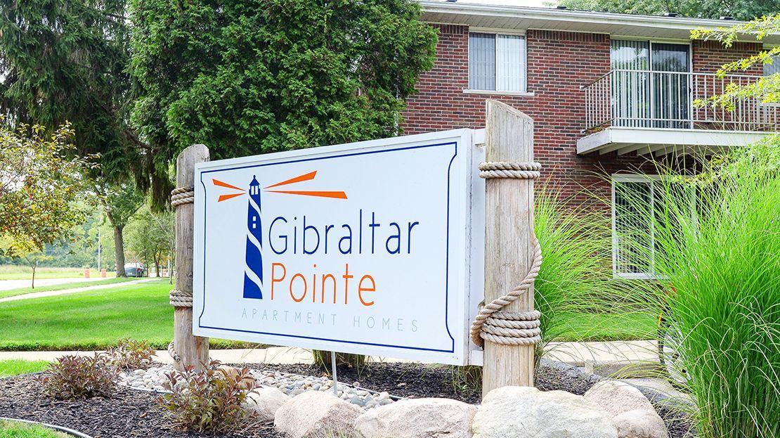 Gibraltar Pointe sign by a brick apartment building, with trees and landscaping nearby