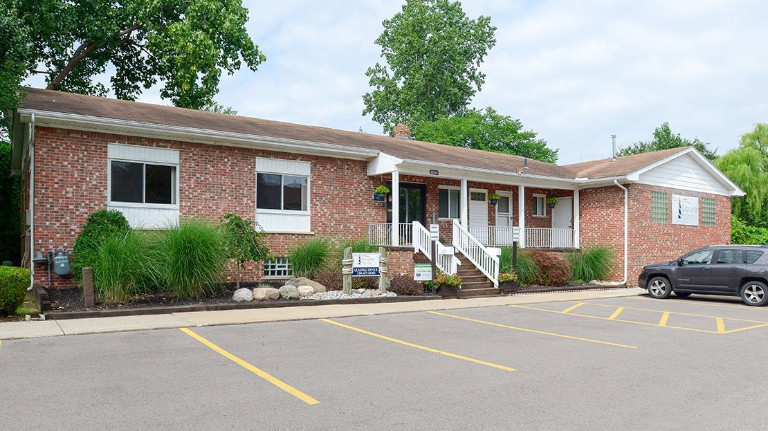 Brick office building with white trim, parking lot, and a few parked cars under trees