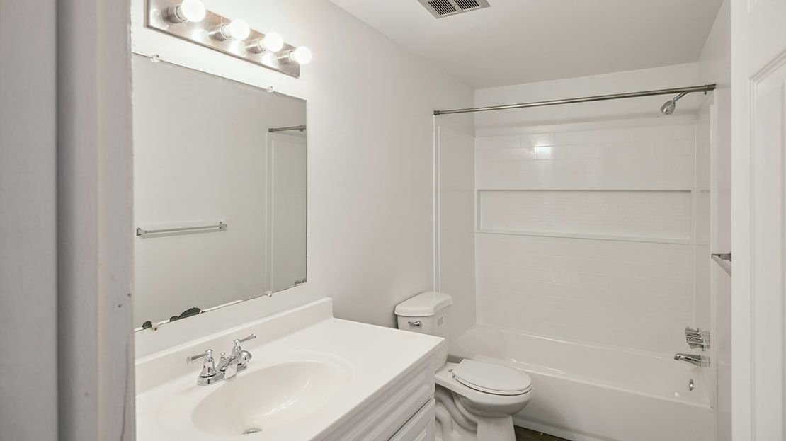 Bright white bathroom with vanity, mirror lights, toilet, and shower/tub combo with curtain rail.