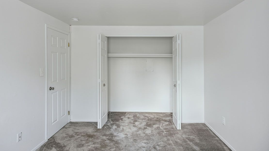 Empty white bedroom with open closet and carpeted floor