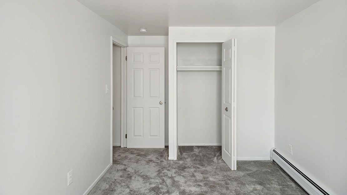 Empty white bedroom with closet, closed door, and gray carpet.